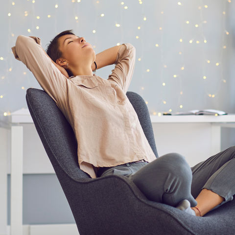 woman with eyes closed and hands behind her head, relaxing in a chair