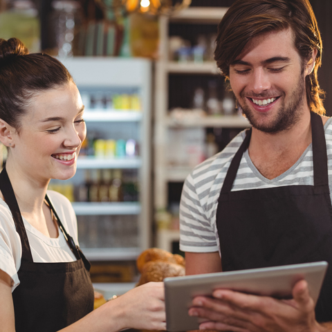 Two hospitality workers, wearing aprons, consulting a tablet, looking happy